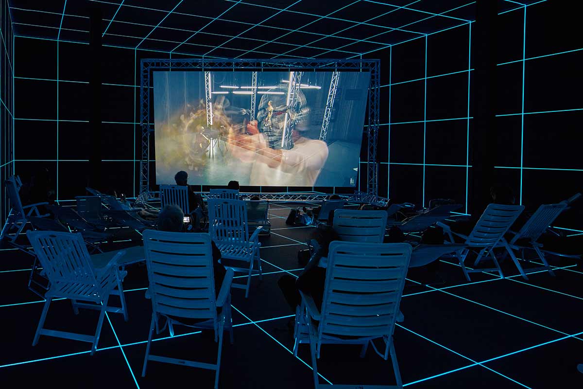 Hito Steyerl. ‘Factory of the Sun’ (installation view). 2015. Single channel high-definition video (colour, sound), environment, luminescent LED grid, beach chairs. Collection of Singapore Art Museum. Image courtesy of the artist, Andrew Kreps Gallery, New York and Esther Schipper, Berlin/Paris/Seoul.